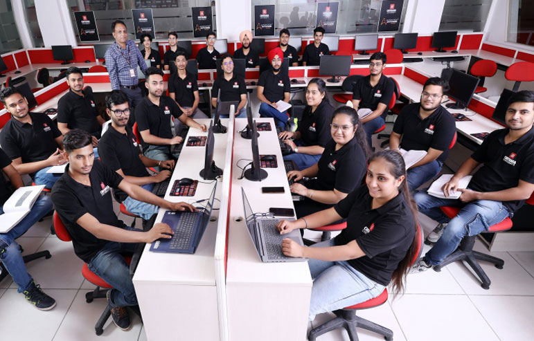The image shows the computer lab of chitkara university with students in black t-shirts sitting in front of the desktops.