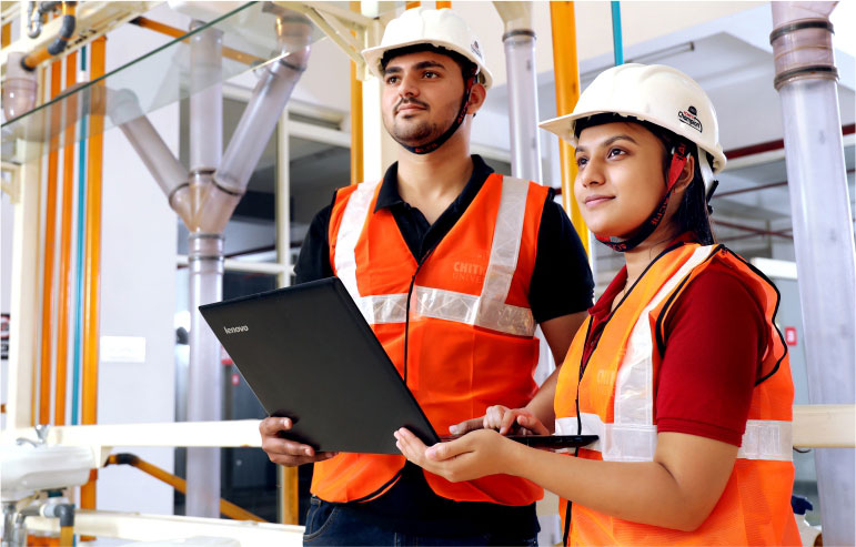 Image with a two engineers one is male and another is female looking of the left side of the image and holding a laptop.