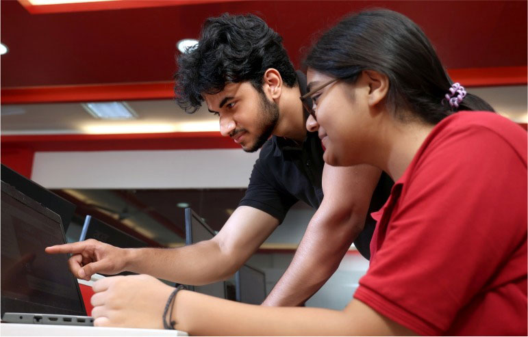The illustration shows the two students of chitkara university. One is a boy in a black t-shirt pointing towards the laptop, and the other is a girl in a red t-shirt looking at the laptop.