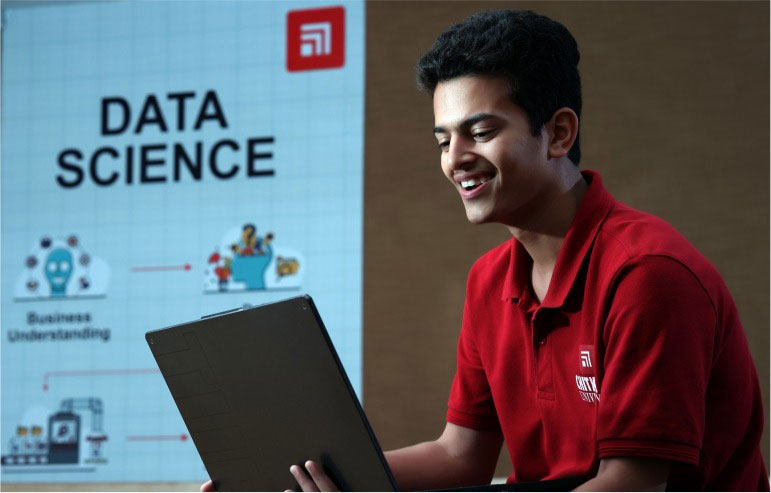 A image with blurred background. On the right side of image Data Science wriiten in black bold text and some symbols are also given below. On the right side of the image student of chitkara university working on their laptop.