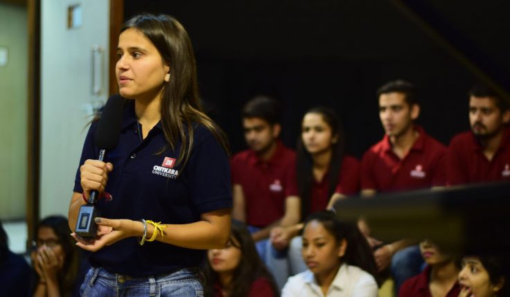 A female student attending a seminar, holding a microphone, and asking questions to seminar guests, showcasing the value of an MA in Journalism & Mass Communication Worth in fostering engagement and inquiry.