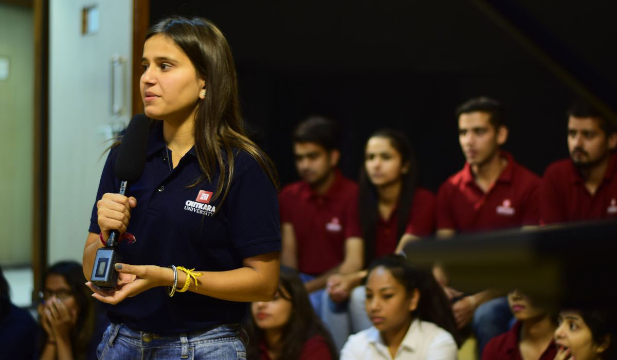 A female student attending a seminar, holding a microphone, and asking questions to seminar guests, showcasing the value of an MA in Journalism & Mass Communication Worth in fostering engagement and inquiry.
