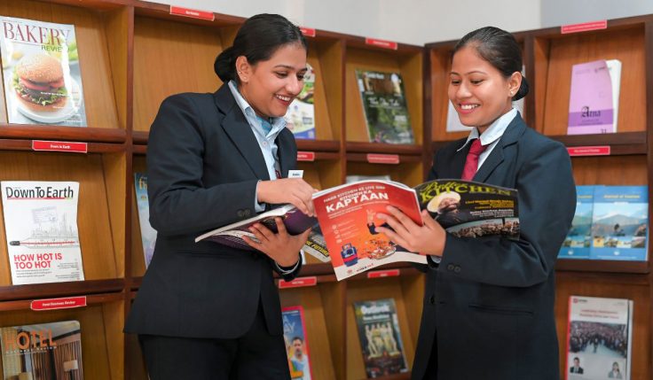 Students enrolled in Professional Baking Courses reading culinary magazines in a library to enhance their knowledge of bakery and pastry arts.