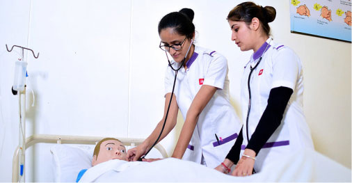 Nursing students using stethoscope on training mannequin during simulation.